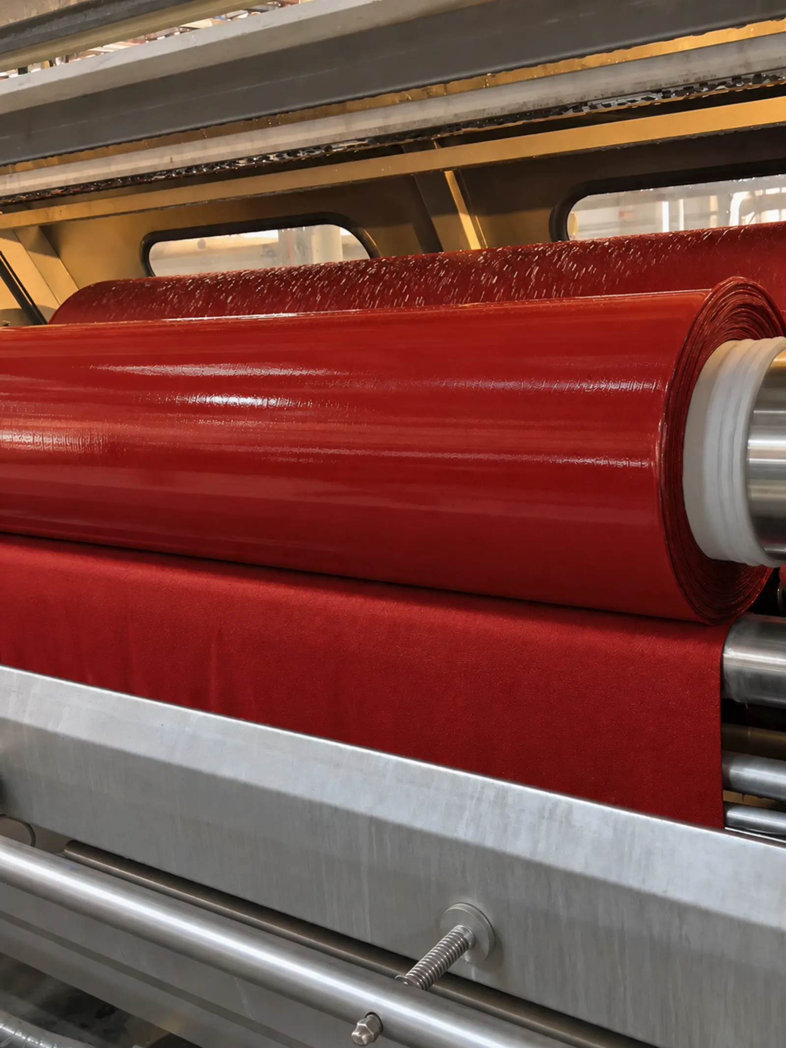 Rolo de tecido tinto em vermelho saindo do equipamento de tingimento.